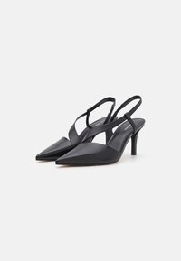 Talons aiguilles en cuir noir à bride arrière, avec un bout pointu, une fine sangle autour de la cheville et un talon stiletto modéré. Texture lisse et design minimaliste.