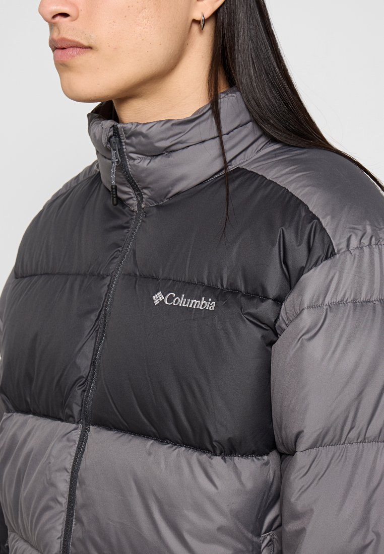 Chaqueta acolchada en tonos de gris con un cuello alto. Presenta un cierre con cremallera en la parte delantera y el logo de Columbia en el pecho. Elaborada con un material texturizado e insulated.
