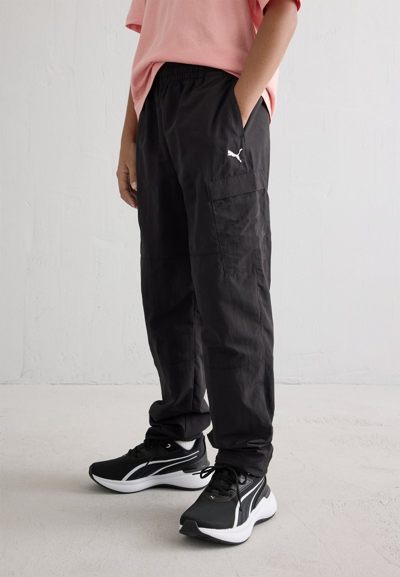 Μαύρο cargo παντελόνι με ελαστική μέση, πλαϊνές τσέπες και λευκό λογότυπο Puma. Συνδυασμένο με μαύρα και άσπρα αθλητικά παπούτσια.
