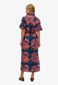 Robe longue bleu marine à motifs floraux rose et orange. Elle présente des manches courtes à volants et une taille ceinturée pour une silhouette ajustée.