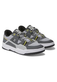 Scarpe da ginnastica grigie e nere con pannelli in rete, dettagli gialli e suole in gomma. Caratterizzate da colli imbottiti e superfici texturizzate.