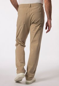 Beżowe spodnie z elastycznym pasem, dwiema tylnymi kieszeniami i luźnym krojem. Noszone z białymi butami, ukazując gładką fakturę i nowoczesny design.