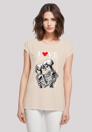 Beige short-sleeve shirt featuring a graphic of two skeletons in an embrace, with text that reads "LOVE IS ALL YOU NEED" in white and red.