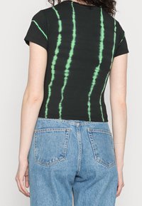 Black short-sleeve t-shirt featuring bright green tie-dye stripes, paired with high-waisted blue denim jeans with back pockets.