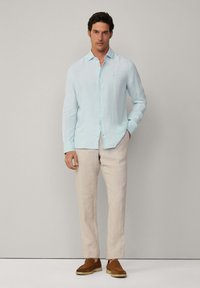 Light blue linen shirt with a button-down collar, paired with beige trousers and brown loafers, featuring subtle texture and no patterns.
