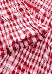 Red and white checkered fabric with gathered texture. Features soft cotton material with a ruffled design. Multi-sized squares pattern.