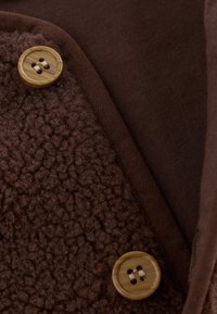 Gros plan d'un tissu texturé brun foncé avec deux boutons ronds en bois cousus avec du fil beige.