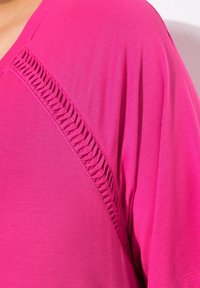 Top fucsia a maniche corte con una cucitura texturizzata e arricciata lungo la spalla. Realizzato in tessuto morbido e leggero con una finitura liscia.