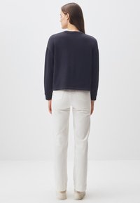 Felpa blu navy con una vestibilità comoda e spalle scese, abbinata a jeans bianchi a gamba dritta e sneakers di colore chiaro.