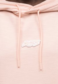 Ανοιχτό ροζ φούτερ με κουκούλα και κορδόνια, με λευκή κεντητή ετικέτα που γράφει "BOSS" στο στήθος.