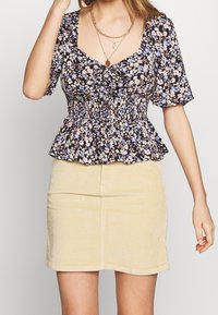 Blusa a fantasia floreale con maniche corte, scollatura quadrata e vita arricciata in nero, rosa e blu. Abbinata a una mini gonna in corduroy beige.