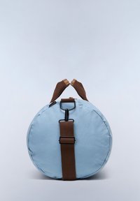 Borsa rotonda azzurro chiaro con tracolla regolabile marrone e guanti senza dita marroni appoggiati sopra, su uno sfondo chiaro e uniforme.
