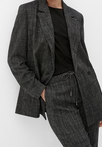 Blazer texturizzato nero e grigio con vestibilità ampia, chiusura a un bottone e revers a punta, abbinato a pantaloni con motivo coordinato.