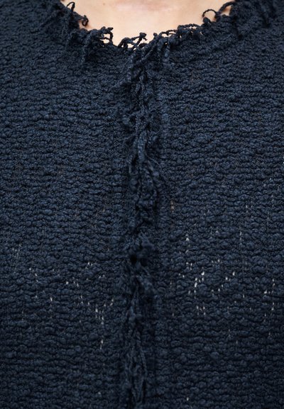 Κοντινό πλάνο σκουρόχρωμου μπλε υφάσματος πλεκτού με υφή, με φθαρμένες άκρες και μια στριμμένη κλωστή στο κέντρο, σε ένδυμα.