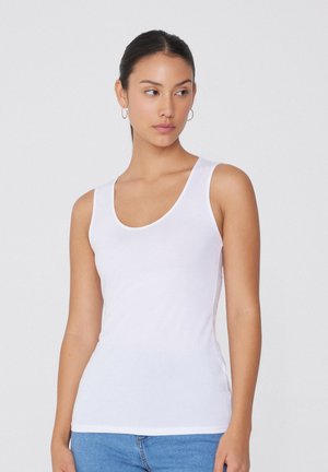 Bílý top bez rukávů vyrobený z hladkého bavlněného materiálu, s výstřihem ve tvaru lodi a slim fit, kombinovaný s džínovými kalhotami pro pohodlný ležérní vzhled.