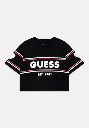 T-shirt court noir avec des rayures blanches et roses, grand texte blanc "GUESS", et "EST. 1981" en dessous à l'avant.