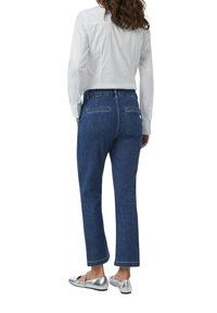 Donkerblauwe jeans met een recht model, voorzien van achterzakken met zichtbare stiksels, gecombineerd met een wit shirt en zilveren flats.
