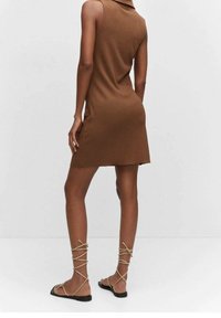 Robe sans manches côtelée marron avec un col montant, présentant une silhouette ajustée et un ourlet juste au-dessus des genoux. Associée à des sandales beiges à lacets.