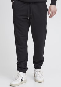 Schwarze Baumwoll-Jogginghosen mit einem elastischen Bund, Kordelzug und gerippten Knöcheln. Tragen Sie dazu weiße Sneakers mit schwarzen Akzenten.