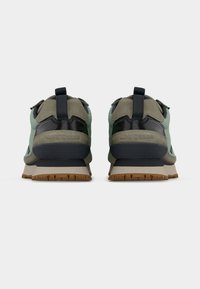 Ζεύγος πράσινων και μαύρων αθλητικών παπουτσιών Converse, εμφανιζόμενα από πίσω, με μπεζ εσωτερικές σόλες και καβουρδισμένες εξωτερικές σόλες σε λευκό φόντο.