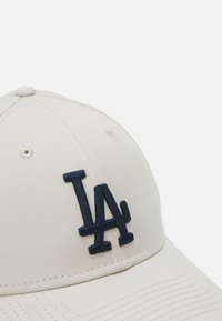 Bejž kapa za bejzbol iz lahkega bombaža s temno modrim vezenim logotipom "LA" spredaj. Ima ukrivljen rob in šivane detajle.