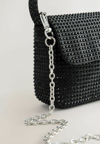 Black rectangular handbag with textured black studs and a silver chain strap attached by a clasp on a light surface.