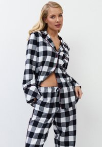Set di pigiama a quadri bianco e nero realizzato in morbido tessuto, con una camicia con colletto e bottoni e pantaloni con vita elastica. Finiture rosse.