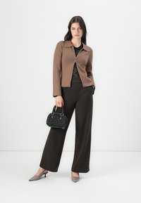Cardigan marrone con zip, top in pizzo nero, pantaloni marroni a gamba larga, décolleté grigie e una piccola borsa nera testurizzata con due manici.