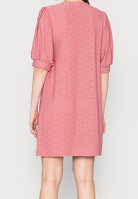 Vaaleanpunainen mekko, jossa on puffi-hihat, reikäkudontaa ja rento malli. Selkäpuolella on yksinkertainen pyöreä pääntie ja polvipituinen helma.