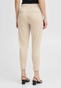 Licht beige joggerbroeken met een slim fit design, elastische tailleband en twee achterzakken. Gecombineerd met zwarte block-heeled sandalen.