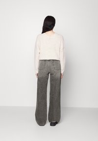 Suéter de color rosa claro y textura suave con escote en V; combinado con jeans de pierna ancha en degradado de negro a gris que cuentan con bolsillos traseros y costuras de contraste.