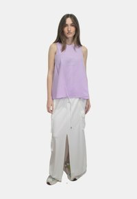 Top senza maniche color lavanda abbinato a una gonna bianca lunga fino al pavimento con cordoncino, spacco frontale e grandi tasche laterali. Le calzature includono scarpe da ginnastica.