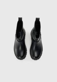 Juodos odinės kulkšnės botai su apvaliu pirštu, elastingomis šoninėmis juostomis ir tekstūruota guma padais. Paprastas dizainas su minimaliais papuošimais.