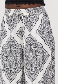 Pantalones de pierna ancha en blanco y negro con patrón, con cintura elástica y cordón. Presentan intrincados diseños de cachemira y diamante.