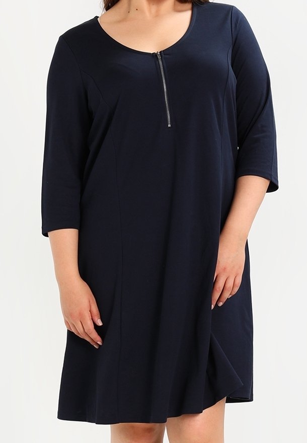 Femme portant une robe bleu marine longueur genou avec manches trois-quarts et zip frontal sur un col rond.