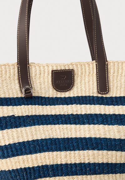 Πλεκτή τσάντα από άχυρο με μπλε οριζόντιες ρίγες, σκούρες καφέ δερμάτινες λαβές και ένα μικρό ραμμένο δερμάτινο έμπλαστρο μπροστά.