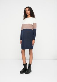 Vestito a maglia con design a blocchi di colore in crema, rosa e blu navy, con maniche lunghe e vestibilità comoda. Abbinato a stivali da combattimento neri.