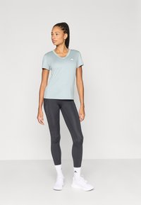 Ανοιχτό μπλε αθλητικό T-shirt με κοντά μανίκια και V-λαιμόκοψη, με λευκό λογότυπο, σε συνδυασμό με ανθρακί κολάν και λευκά αθλητικά παπούτσια.