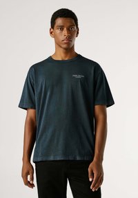 Crna pamučna majica kratkih rukava, okruglog izreza i malim bijelim logom na prsima. Ležeran kroj i glatka tekstura.