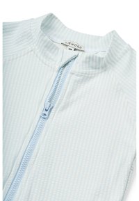 Light blue zip-up top featuring a textured, striped pattern. The collar is round, and the zipper is in a matching hue, designed for comfort.