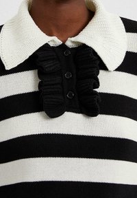 Sort-hvid stribet strikket polo-shirt med en struktureret cremefarvet krave, flæset frontstykke og sorte knapper.