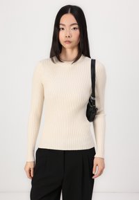 Ribbed, cream sweater with a high neck and long sleeves, paired with black trousers and a small black shoulder bag.