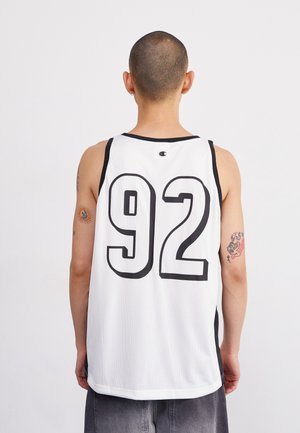 Person mit kurzen Haaren, die ein weißes ärmelloses Sporttrikot mit der Nummer 92 trägt, Rückenansicht, mit tätowierten Armen und grauen Shorts.