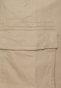 Un tissu beige clair avec une texture lisse présente une poche avant rectangulaire et des coutures contrastantes le long des coutures.