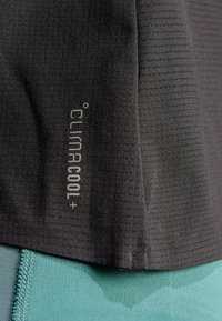 Sort performance-shirt med tekstureret stof, der har et "ClimaCool+" logo. Skjorten har en glat overflade og passer sammen med et baselag i teal-farve.