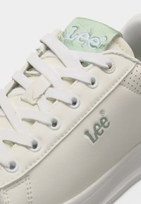 Λευκό αθλητικό παπούτσι της μάρκας White Lee με λευκά κορδόνια, πράσινη επένδυση στην ετικέτα της γλώσσας και διάτρητες λεπτομέρειες κοντά στη φτέρνα.