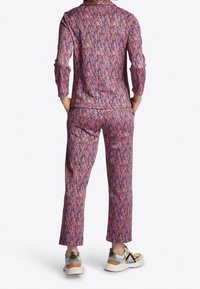 Multikleurige loungewear set met een geometrisch ontwerp in roze, paars en oranje; losse pasvorm met lange mouwen en broek die tot de enkels reikt.