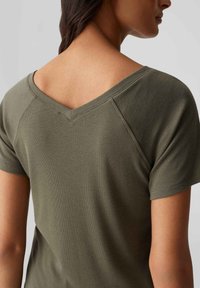 Olivgrünes kurzärmliges Hemd mit einem strukturierten Rippdesign und einem V-Ausschnitt. Verfügt über Raglanärmel für einen entspannten Schnitt.