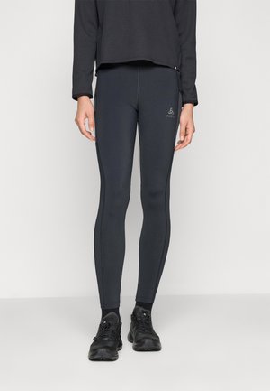 Black fitted leggings made of stretchy material, featuring a logo on the front and a smooth texture, paired with black athletic shoes.