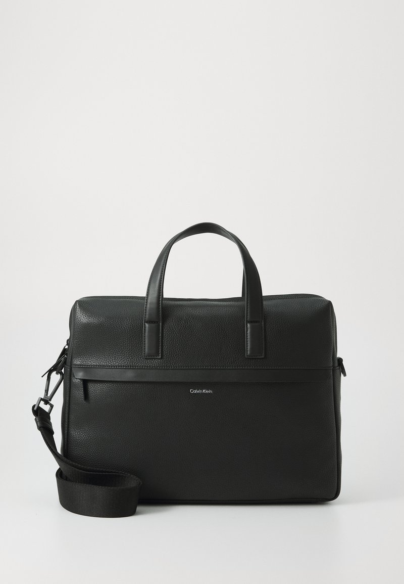 Black leather briefcase with textured finish, dual top handles, adjustable shoulder strap, and a horizontal zip pocket on the front.